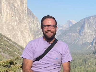 Dr. Alex Sutton, lecturer in global change ecology at Bangor University in Wales standing in mountain meadow with mountains in background